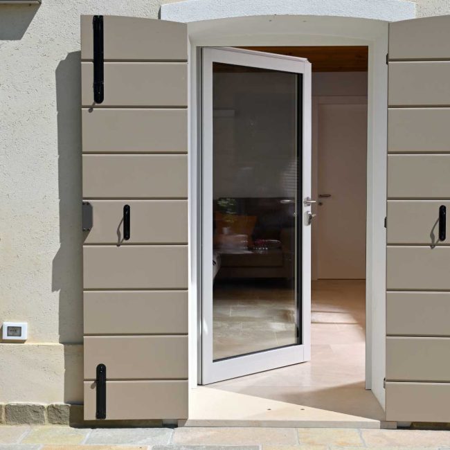 Particolare dello scuro a scandole laccato ad arco e portoncino a vetro con rivestimento in alluminio RAL 9010.