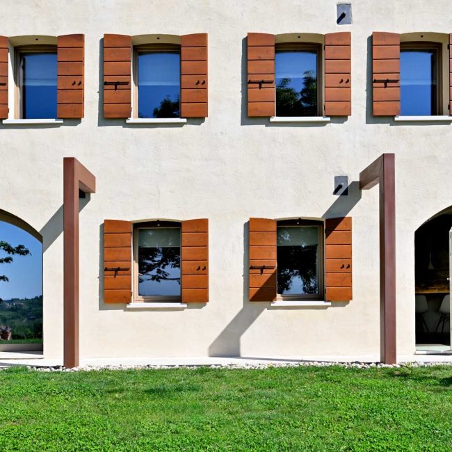 Fornitura scuri a scandole in abete e finestre in pino di Svezia lamellare spazzolato. Porte finestre ad arco con apertura a bilico verticale.