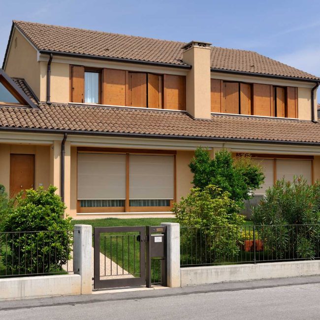 Bifamiliare in zona residenziale con scuri, tamponamenti in legno e tende motorizzate.
