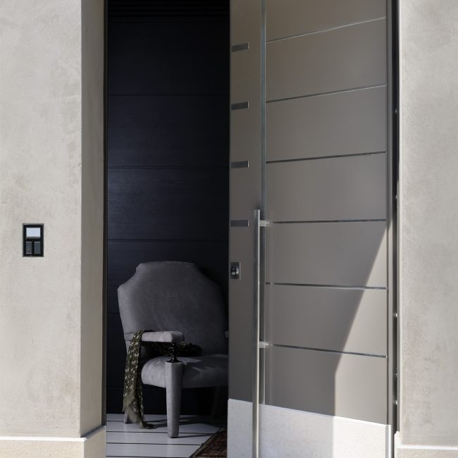 Portoncino blindato a disegno con intarsi e maniglione in acciaio inox e zoccolo in marmo.