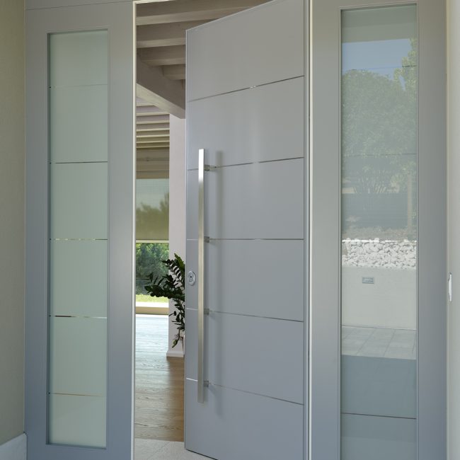 Portoncino blindato laccato con maniglione e inserti in acciaio inox, parti laterali in vetro satinato con righe trasparenti.